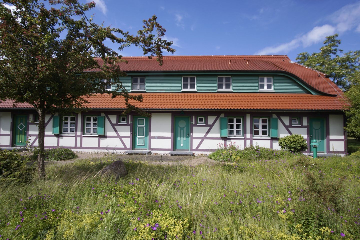 A traditional half-timbered house with a red-tiled roof, green shutters, and a symmetrical facade.