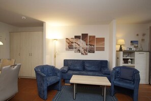 A living room with a blue sofa set, a wooden coffee table, and a floor lamp. There is a wall-mounted artwork above the sofa.