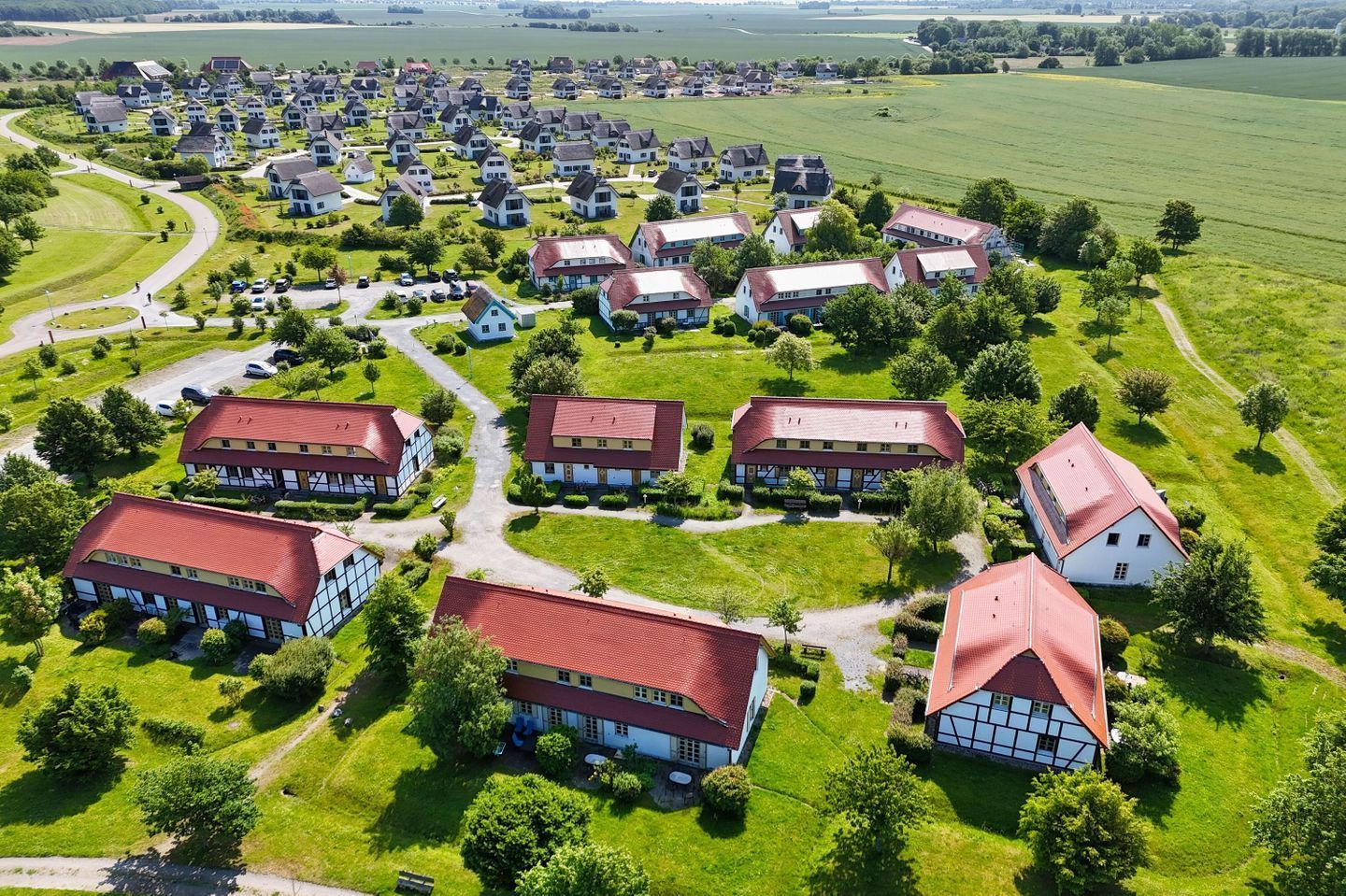 An aerial view of a residential area with multiple houses, each featuring a red roof and a mix of white and dark-colored walls.