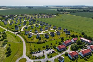 An aerial view of a residential area with houses arranged in a circular pattern, surrounded by green fields and a few larger buildings with red roofs.