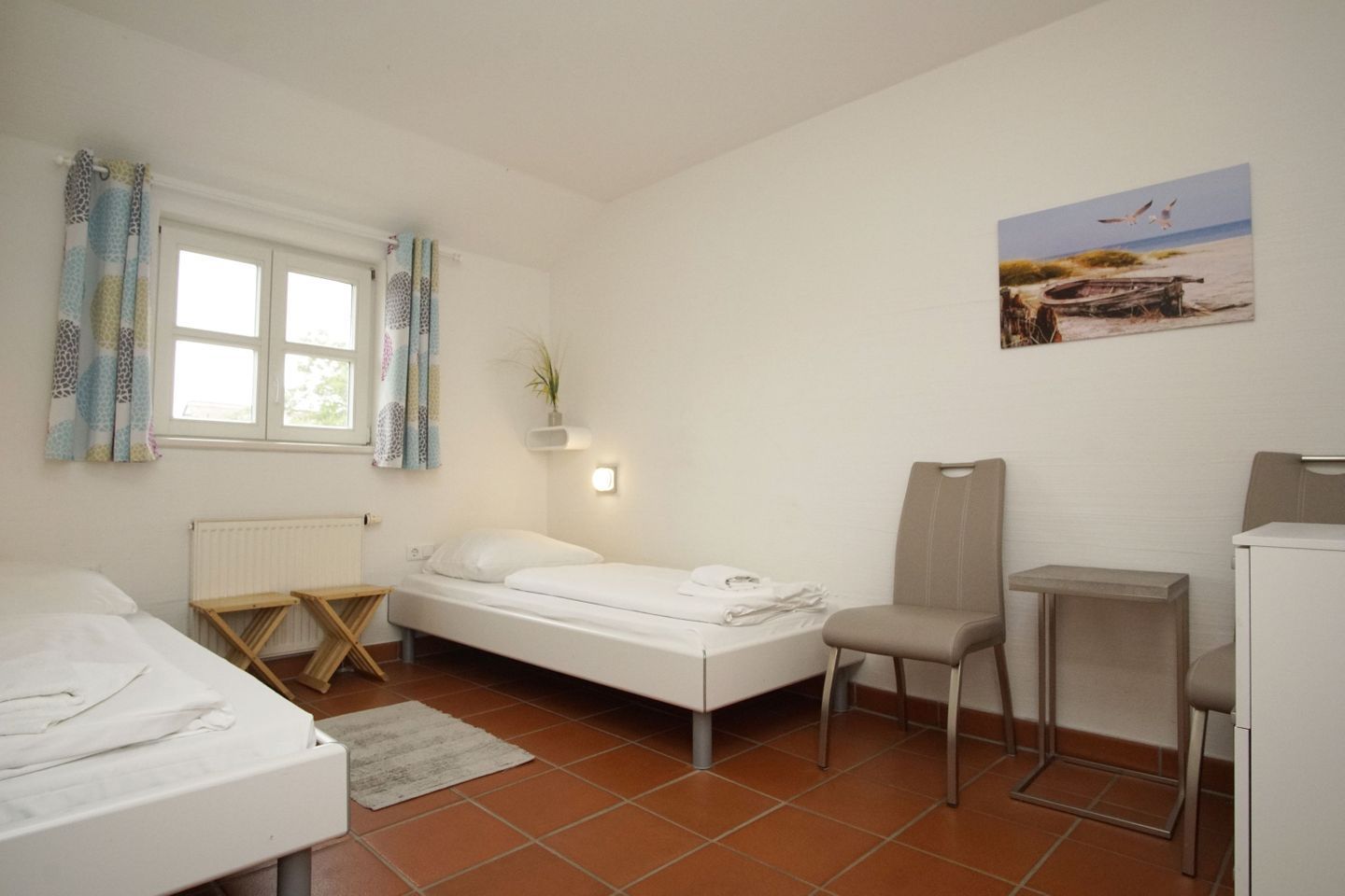 Une petite pièce propre, avec un lit, une chaise, un bureau et une fenêtre avec des rideaux.