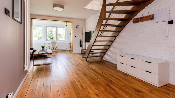 Une pièce spacieuse avec un plancher en bois, un mur en briques blanches, un escalier en bois et une armoire blanche.