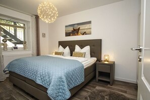 A bedroom with a large bed, a nightstand with a lamp, a window with curtains, a staircase, and a painting on the wall. - Residence Waldidyll FeWo Lieblingsplatz - modern vacation apartment in a quiet location - (Sellin)