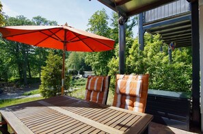 An outdoor patio with a wooden table and two striped chairs, an orange umbrella, and a view of a garden and trees. - Residence Waldidyll FeWo Lieblingsplatz - modern vacation apartment in a quiet location - (Sellin)