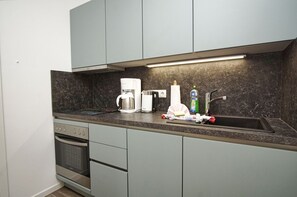 Cozinha compacta com forno embutido, máquina de café e pia.