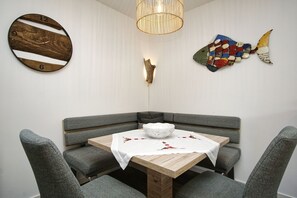 A corner dining area with a wooden table, grey upholstered chairs, a white tablecloth, and a decorative fish wall art piece. - Residence Waldidyll FeWo Lieblingsplatz - modern vacation apartment in a quiet location - (Sellin)
