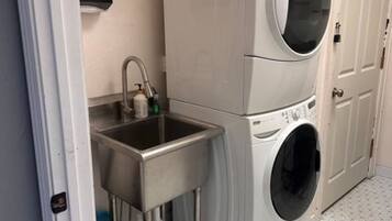 Un espace buanderie comprenant un lave-linge et un sèche-linge superposés, un évier et une petite poubelle.