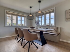 A modern dining area with a wooden table, cushioned bench seating, and pendant lighting.