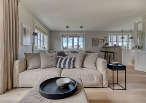 A modern living room with a beige sofa, a black tray with a bowl, and a dining area with a bar.