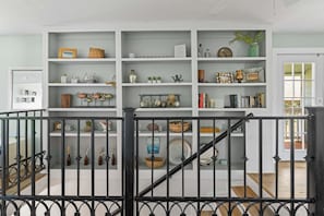 A white interior with a staircase, a bookshelf with various decorative items, and a black railing.