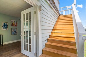 A wooden staircase leading to a white door with glass panels, a light green wall with framed artwork, and a clear blue sky.