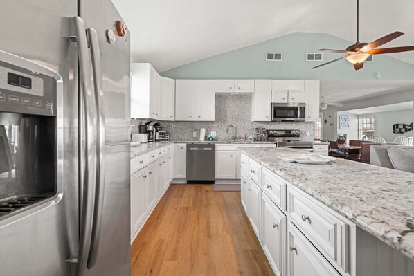A modern kitchen with white cabinets, stainless steel appliances, and a marble countertop.