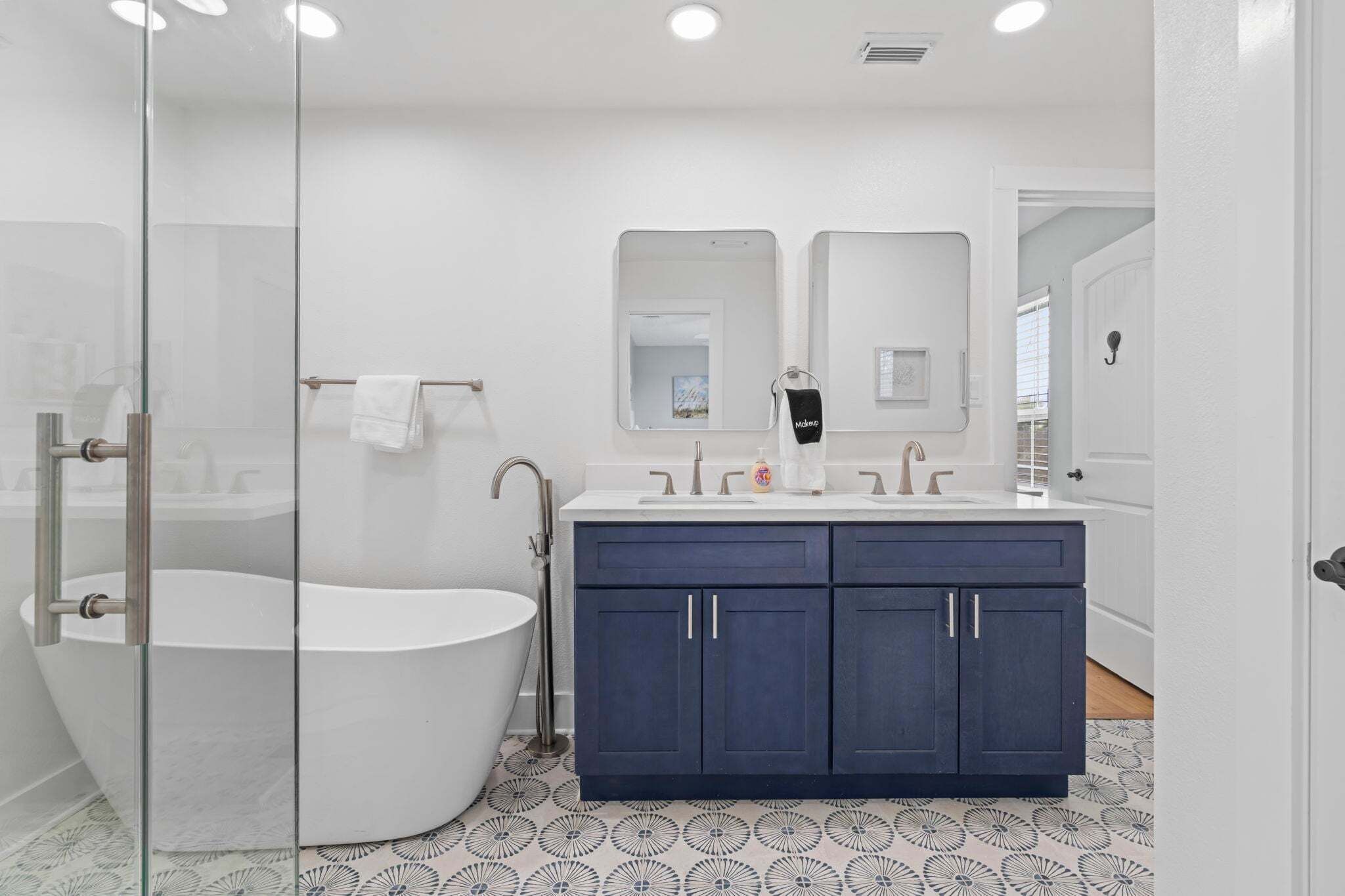 A modern bathroom with a freestanding bathtub, a double vanity with dark cabinets, and a glass shower enclosure.