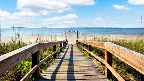 Une promenade en bois mène à une plage où un panneau indique « RUE BYERS ».