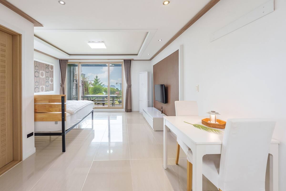 A modern hotel room with a bed, a desk, a TV, and a balcony with a view.