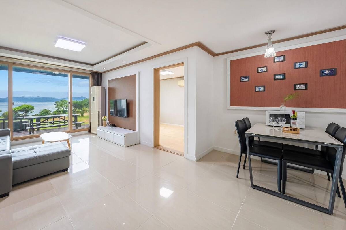 A modern living room with a sofa, a dining table with chairs, a TV, and a view of the outdoors.