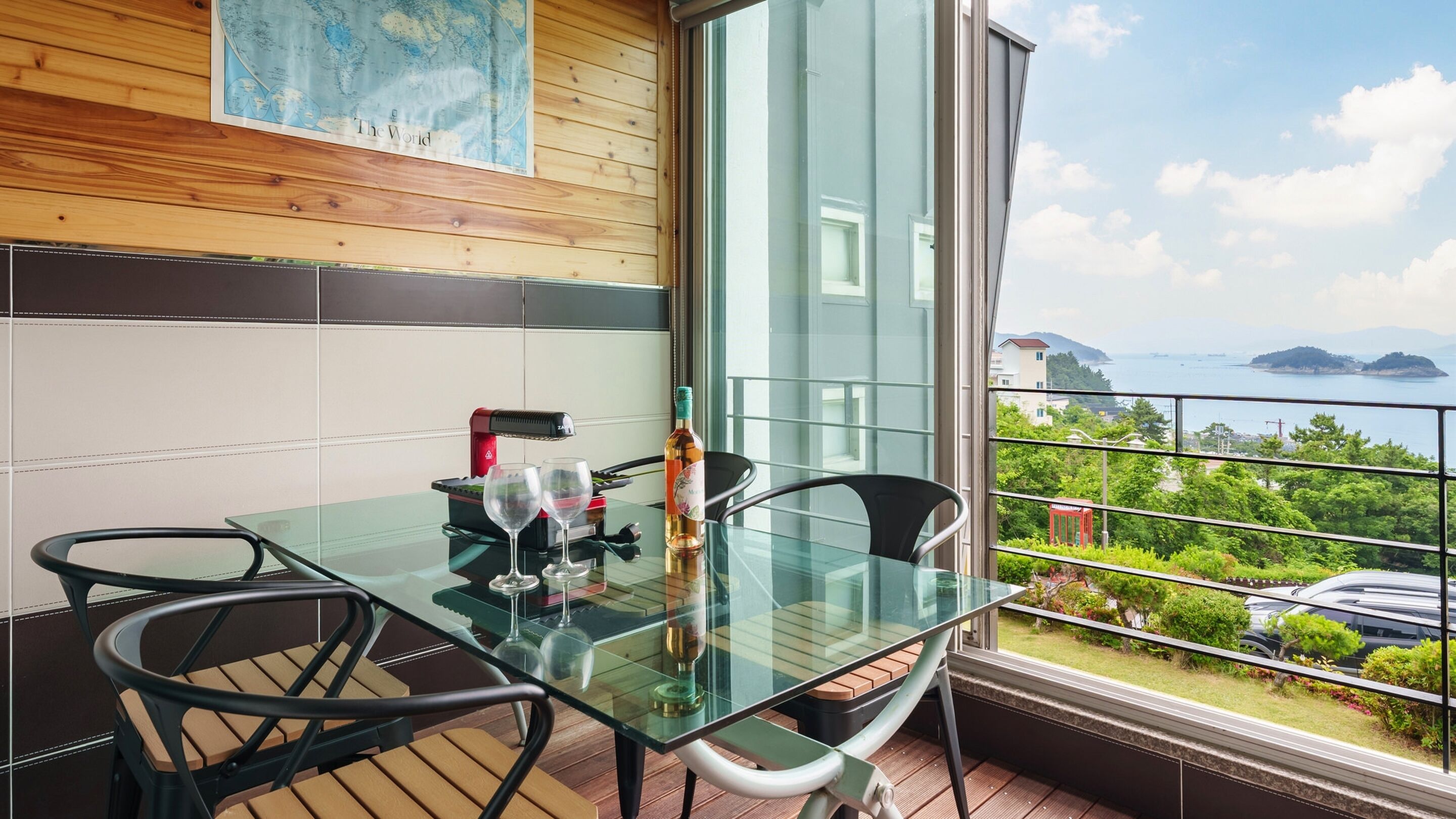 A balcony with a glass table, two chairs, a bottle, and a glass.