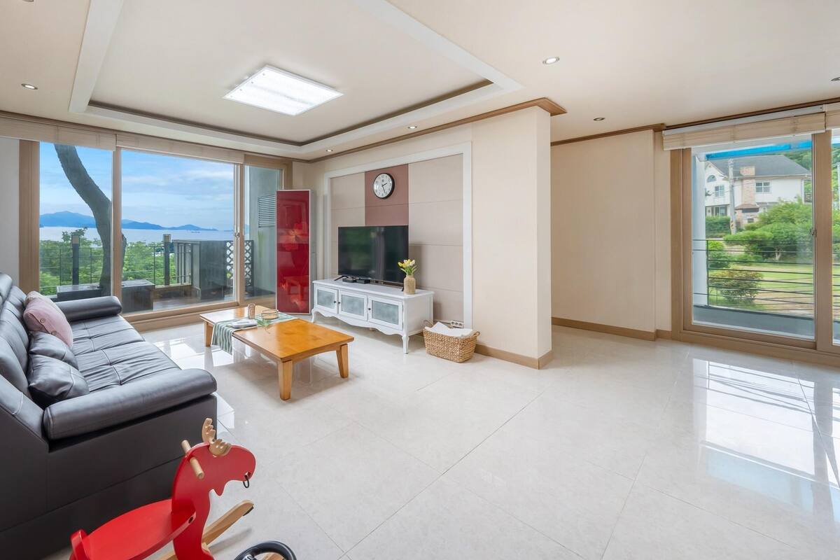 A spacious living room with a black sofa, a wooden coffee table, and a red toy horse.