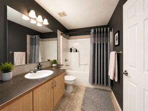 A modern bathroom with a large mirror, two sinks, a toilet, a bathtub, and a shower curtain.