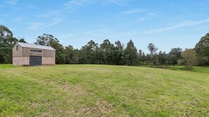 A rustic barn with a brick base and wooden upper structure, surrounded by a grassy field and dense trees. - Meadow Mist - Kangaroo Valley (Kangaroo Valley)