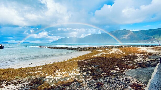 A beach with a rocky shoreline, a boat, and a mountain range in the background. - Casa Marina 4-bed Villa With Pool in Famara (Teguise)