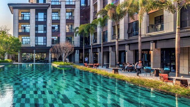 Un hotel moderno con una amplia piscina al aire libre, varios balcones y zonas de estar exteriores.