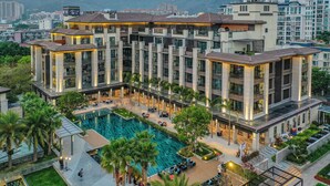 Un hotel moderno con varios pisos, un patio central con piscina y zonas verdes circundantes.