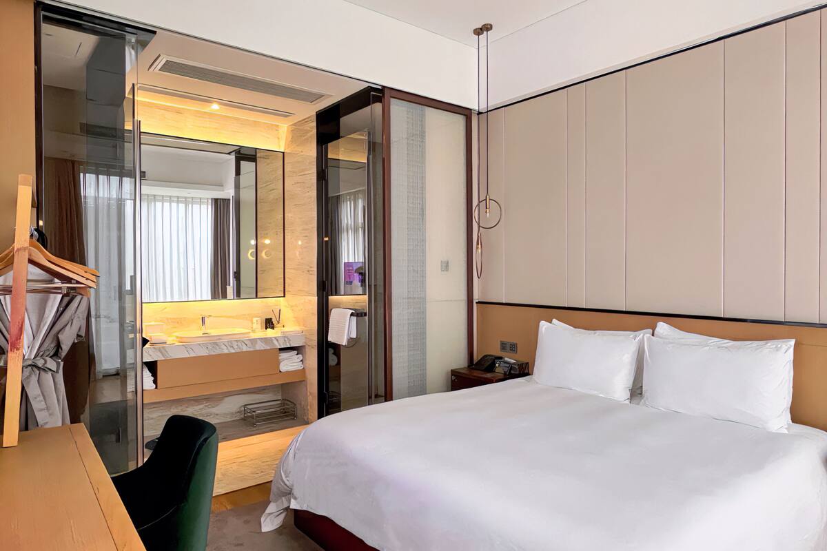 A hotel room with a bed, a desk, a chair, a vanity with a mirror, and a wardrobe.