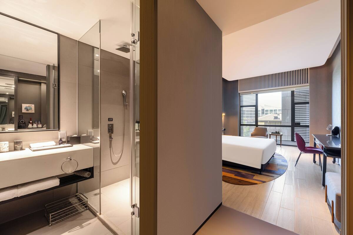 A modern hotel room with a large bed, a desk, and a shower area.