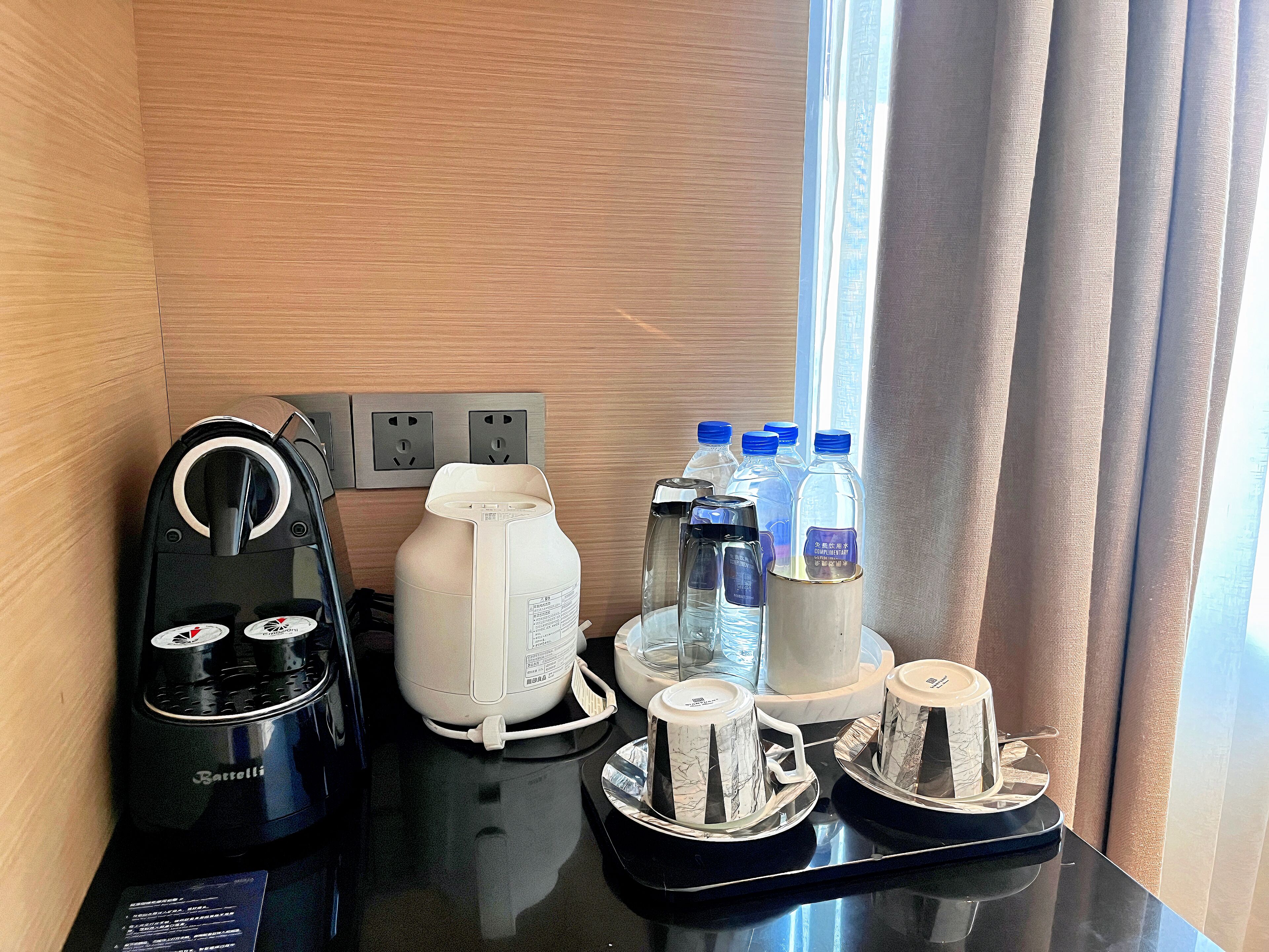 Hotellihuone, jossa on kahvinkeitin, vesiautomaatti sekä tarjotinalus kuppeineen ja pulloineen.