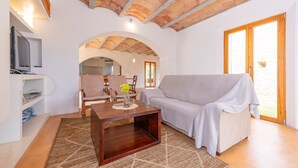 Ein Wohnzimmer mit Couch, Fernseher auf einer Ablage und einem Holztisch.