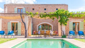 Ein Steinhaus mit Swimmingpool, Außenbereich und einer Pergola mit Weinreben.