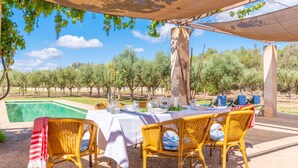 Ein Essbereich im Freien mit Korbstühlen und einem Tisch für zwei Personen, mit Blick auf einen Pool und einen Weinberg.