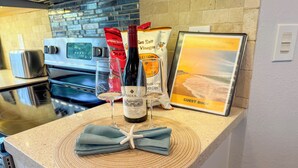 Uma bancada de cozinha com uma garrafa de vinho, dois copos, uma estrela-do-mar e um livro de visitas sobre um descanso de palha.
