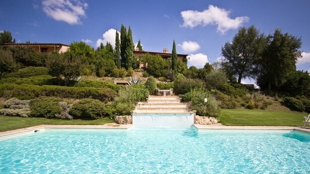 A swimming pool with clear blue water, surrounded by lush greenery and a stone staircase leading up to a building. - Villa La Cascata with swimming pool (Chiusi)