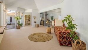 A spacious living area with a large sofa, a round rug, and potted plants. - Colonial Modern Villa Sleep 14-Pool, Palapa, Court (Noord)