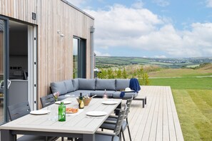 Ein Essbereich im Freien mit einer Holzterrasse, einem grauen Sofa und einem Tisch für zwei Personen.
