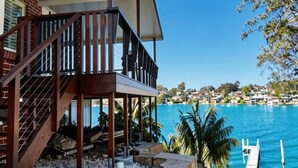 A modern house with a wooden staircase, a balcony, and a view of a blue body of water.