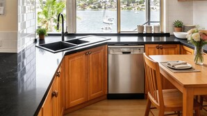 A kitchen with a view of a marina, wooden cabinets, a black countertop, and a dishwasher.