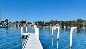 A wooden pier extending into clear blue water with boats docked nearby.