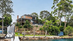 A waterfront property with a dock, a house with a balcony, and surrounding greenery.