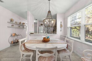 A dining area with a round table, white chairs, a chandelier, and shelves with decorative items. - Updated1 Beautiful Decor! Walk to Beach & Eats (St. Augustine)