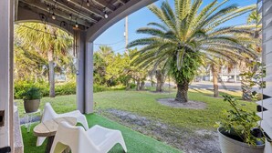 A covered outdoor seating area with artificial grass, white plastic chairs, and a palm tree. - Updated! Beautiful Decor! Walk to Beach & Eats (St. Augustine)