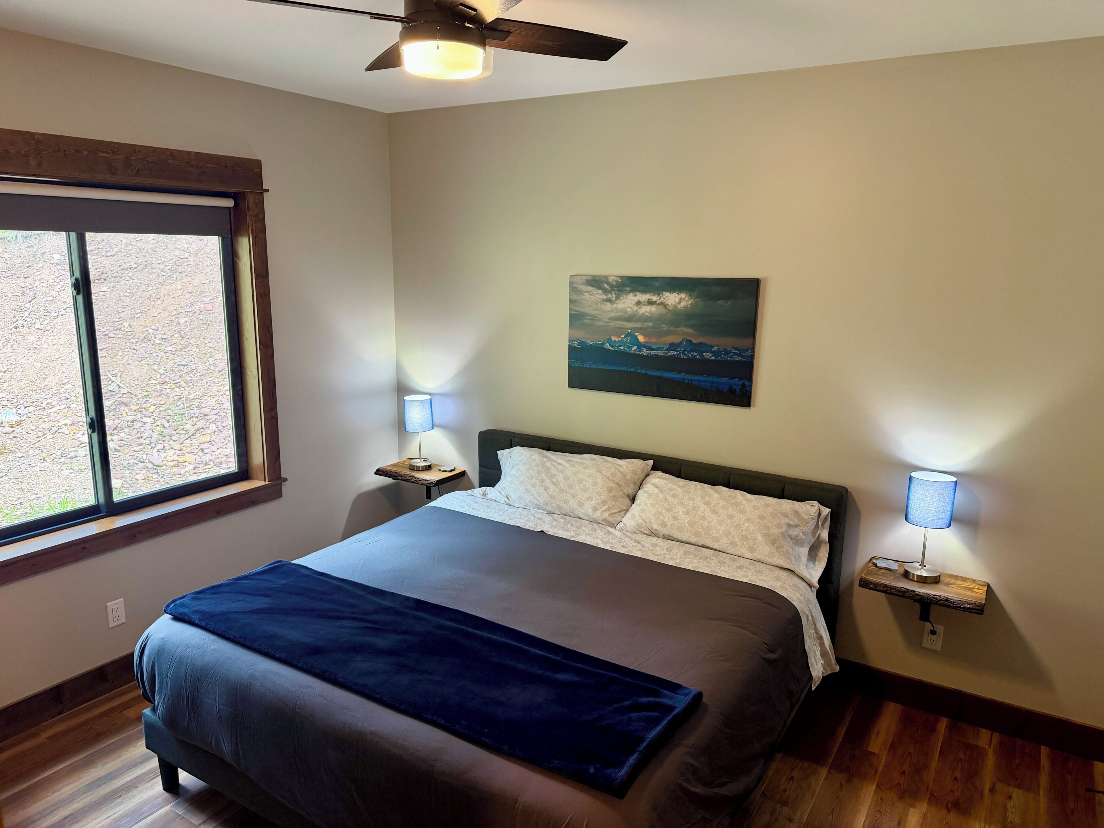 Une chambre à coucher avec un lit, un ventilateur de plafond, un tableau et deux lampes de chevet.