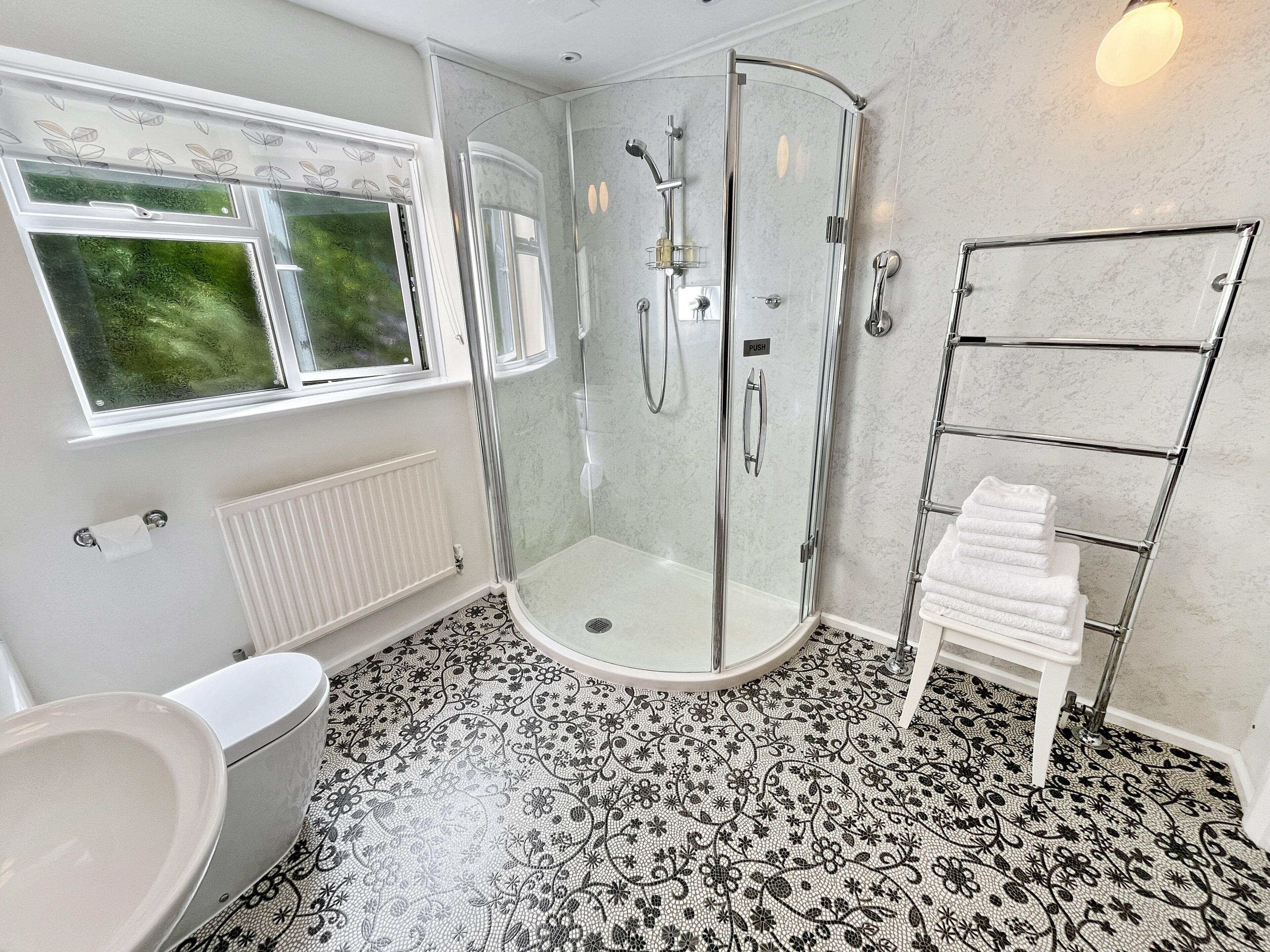 Un baño con cabina de ducha de vidrio, inodoro, lavamanos y perchero para toallas.