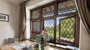 A dining table set for two with a vase of flowers, a bottle of wine, and a scenic view through the window. - Gamekeeper's Cottage near Martinhoe (Parracombe)