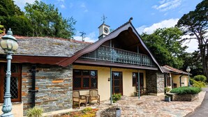A stone house with a balcony, a clock tower, and a garden area. - Gamekeeper's Cottage near Martinhoe (Parracombe)