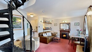 A spacious living room with a fireplace, a striped sofa, a dining table, and a staircase. - Gamekeeper's Cottage near Martinhoe (Parracombe)