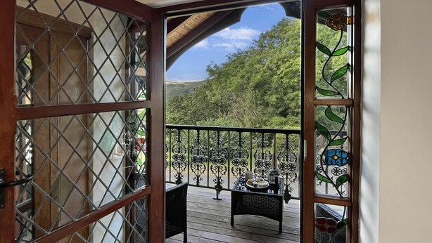 A wooden deck with a metal railing, a table with chairs, and a view of a forested hillside. - Gamekeeper's Cottage near Martinhoe (Parracombe)
