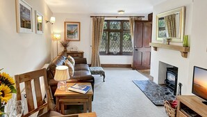 A cozy living room with a sofa, a wooden table with a loaf of bread, a lamp, and a television. - Gardener Cottage near Martinhoe (Parracombe)